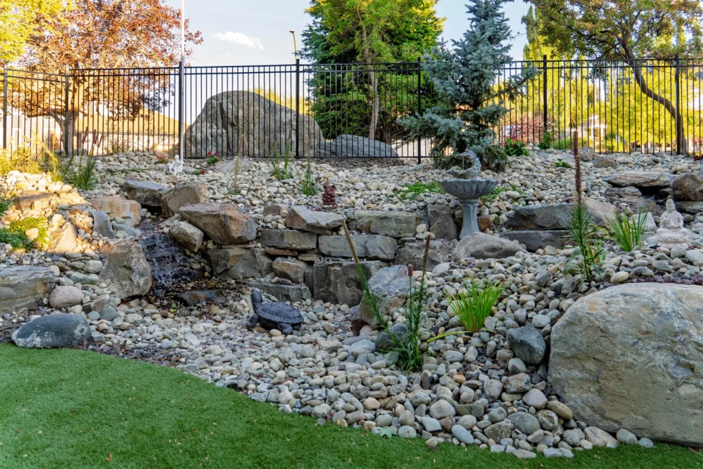 Stone stream cascade with river rock and a large boulder beside the turf area