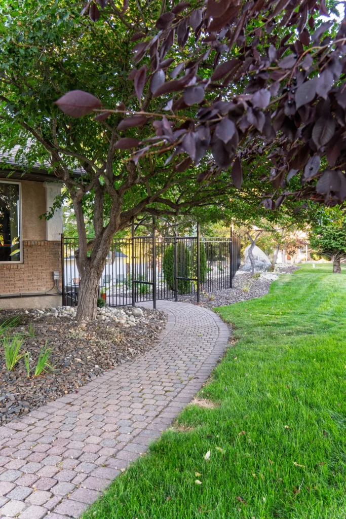 Curving paver walkway beneath mature trees toward the arbor gate